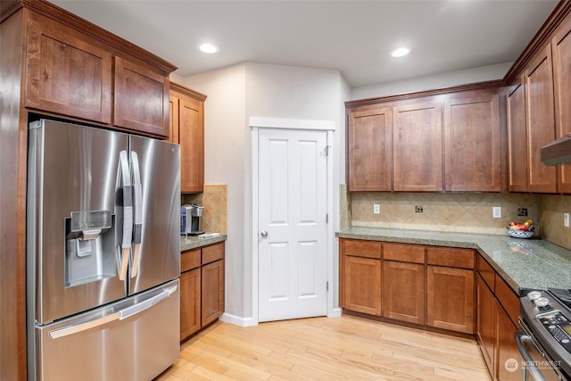 kitchen featuring tasteful backsplash, appliances with stainless steel finishes, light stone counters, and light wood-type flooring