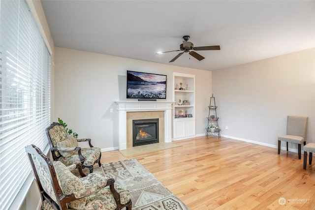 living room featuring a fireplace, light hardwood / wood-style flooring, built in features, and ceiling fan