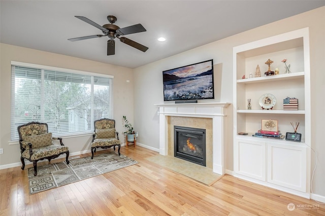 living area with a tiled fireplace, built in shelves, light hardwood / wood-style floors, and ceiling fan