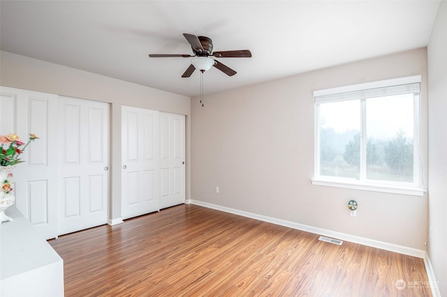 unfurnished bedroom with hardwood / wood-style flooring, two closets, and ceiling fan