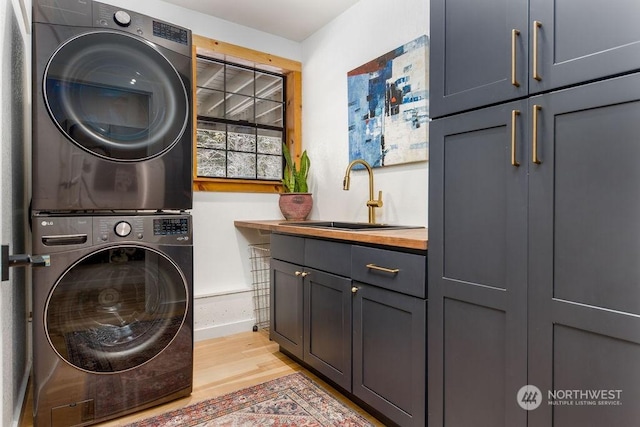 laundry area featuring cabinets, stacked washing maching and dryer, sink, and light hardwood / wood-style flooring