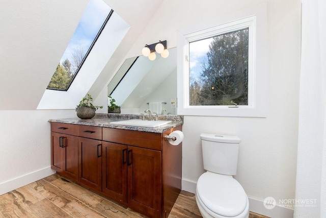 bathroom with vanity, wood-type flooring, vaulted ceiling with skylight, and toilet