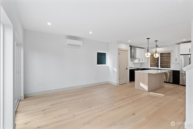 kitchen featuring wall chimney range hood, appliances with stainless steel finishes, a wall mounted air conditioner, a kitchen island, and decorative light fixtures