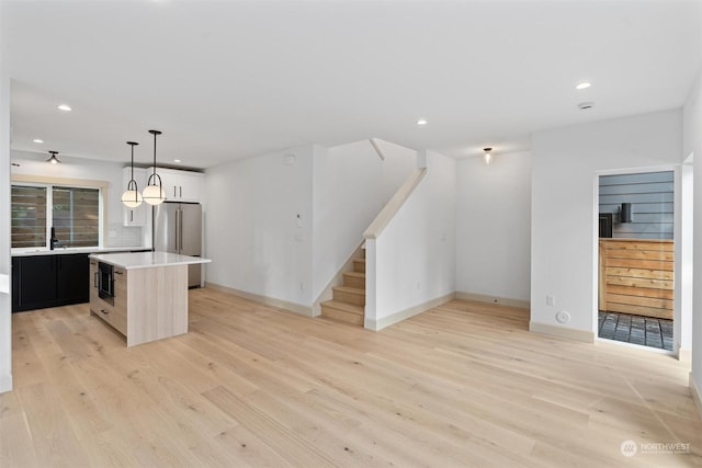 kitchen with hanging light fixtures, backsplash, a kitchen island, high end refrigerator, and light wood-type flooring