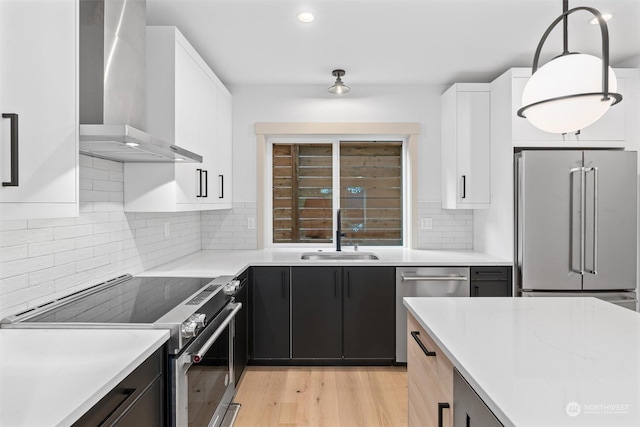 kitchen featuring wall chimney exhaust hood, sink, hanging light fixtures, stainless steel appliances, and white cabinets