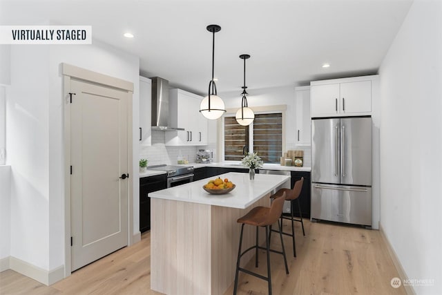 kitchen featuring appliances with stainless steel finishes, hanging light fixtures, a center island, white cabinets, and wall chimney exhaust hood