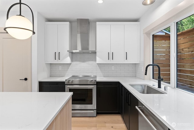 kitchen with appliances with stainless steel finishes, wall chimney exhaust hood, light stone countertops, and sink