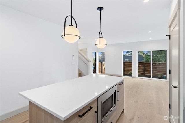 kitchen with a wealth of natural light, stainless steel microwave, decorative light fixtures, a center island, and light hardwood / wood-style flooring