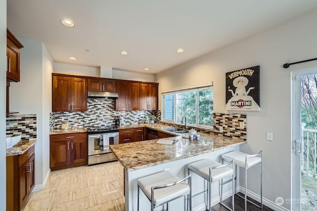 kitchen with sink, a breakfast bar area, light stone counters, stainless steel electric range oven, and kitchen peninsula