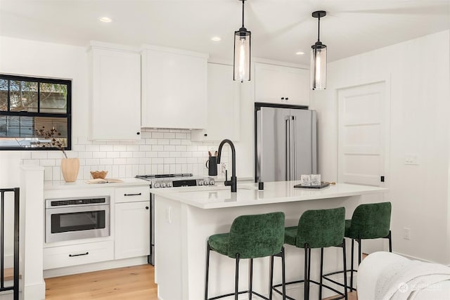 kitchen featuring appliances with stainless steel finishes, decorative light fixtures, an island with sink, white cabinets, and backsplash