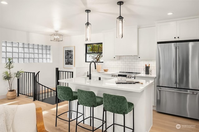 kitchen with stainless steel fridge, decorative light fixtures, a kitchen island with sink, and white cabinets