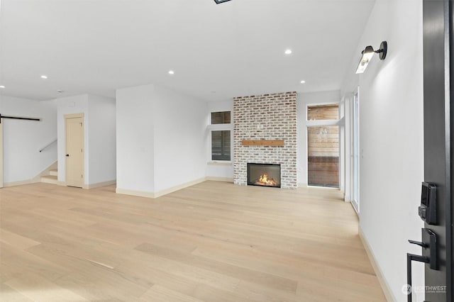 unfurnished living room with a large fireplace, a barn door, and light wood-type flooring