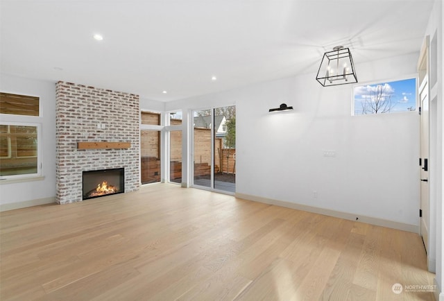 unfurnished living room featuring a chandelier, a brick fireplace, and light wood-type flooring