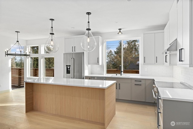 kitchen with sink, white cabinetry, premium appliances, a kitchen island, and decorative light fixtures