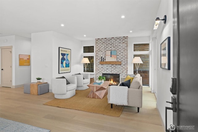 living area featuring baseboards, recessed lighting, a brick fireplace, and light wood-style floors