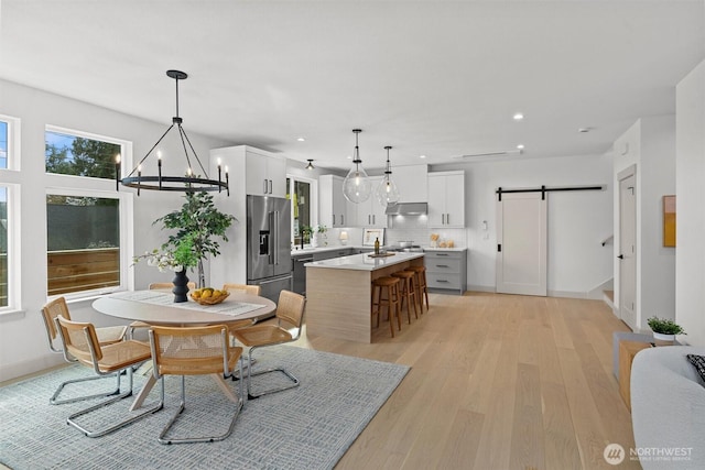 kitchen with high quality fridge, a barn door, under cabinet range hood, light countertops, and a center island with sink