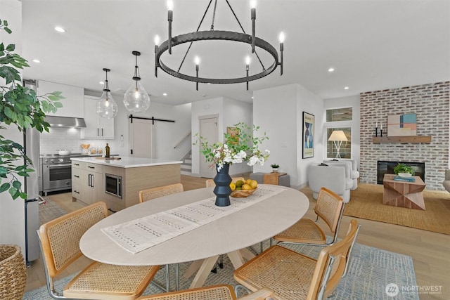 dining area featuring light wood finished floors, a barn door, a fireplace, a notable chandelier, and recessed lighting