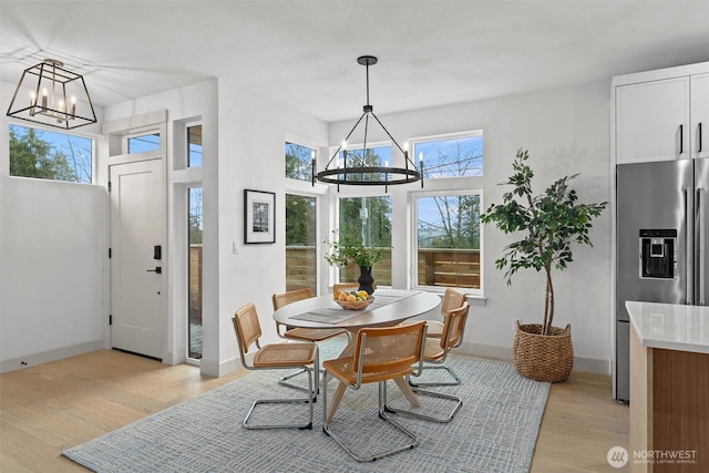 dining area with baseboards, light wood finished floors, a high ceiling, and an inviting chandelier