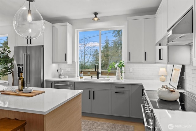 kitchen featuring light stone counters, stainless steel appliances, gray cabinetry, a sink, and ventilation hood