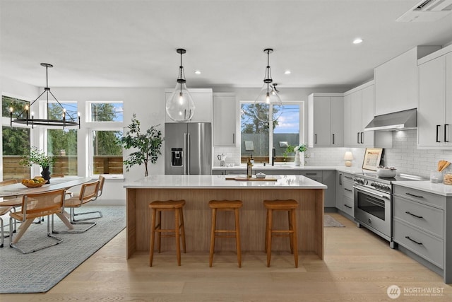 kitchen featuring premium appliances, light countertops, gray cabinetry, a kitchen island with sink, and exhaust hood