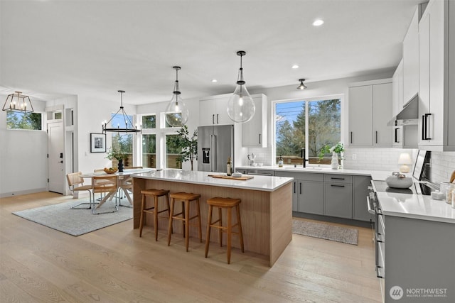 kitchen with stainless steel appliances, gray cabinetry, a kitchen island, under cabinet range hood, and a kitchen breakfast bar