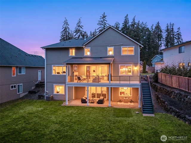 back of house at dusk featuring a patio, a lawn, central AC unit, fence, and stairs