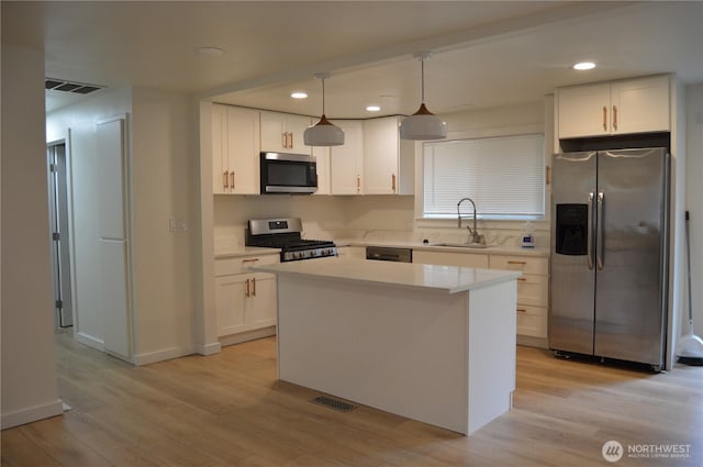 kitchen featuring stainless steel appliances, a sink, white cabinetry, light countertops, and pendant lighting