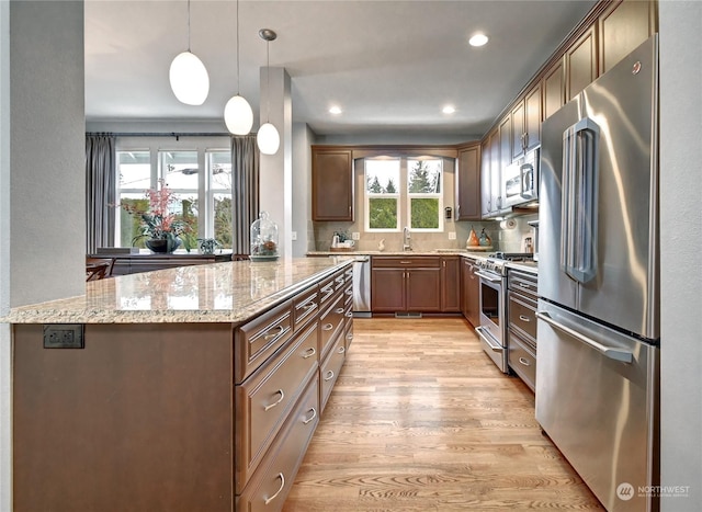 kitchen featuring high end appliances, plenty of natural light, pendant lighting, light stone countertops, and light hardwood / wood-style floors