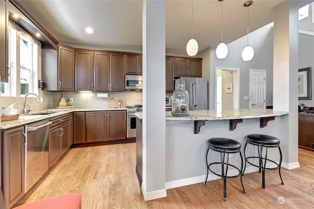 kitchen with sink, light hardwood / wood-style flooring, appliances with stainless steel finishes, pendant lighting, and decorative backsplash