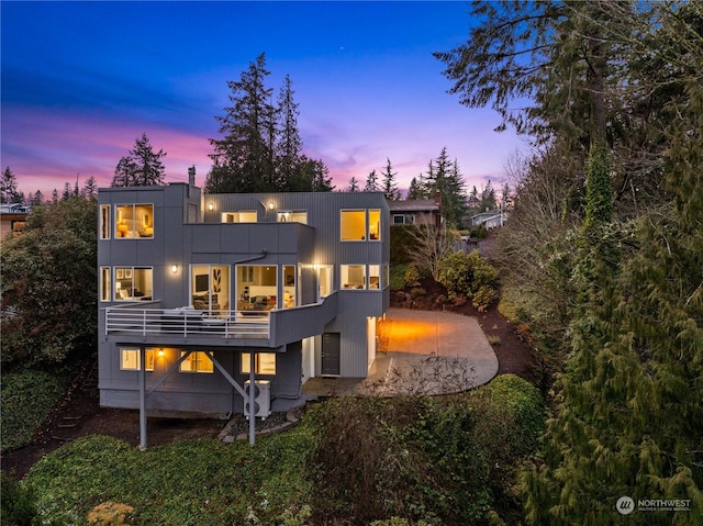 back house at dusk with a balcony and a patio