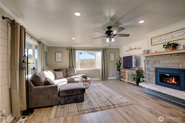 living room featuring crown molding, a stone fireplace, ceiling fan, and light wood-type flooring