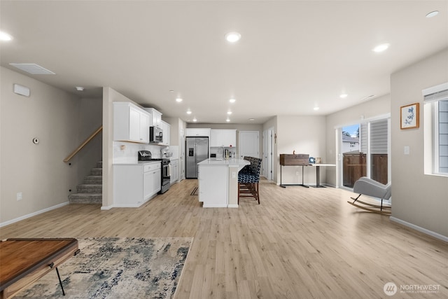kitchen featuring appliances with stainless steel finishes, a kitchen bar, light wood-style flooring, and white cabinetry