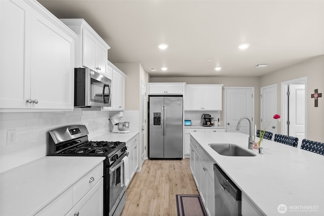 kitchen with white cabinets, appliances with stainless steel finishes, a sink, light wood finished floors, and light countertops