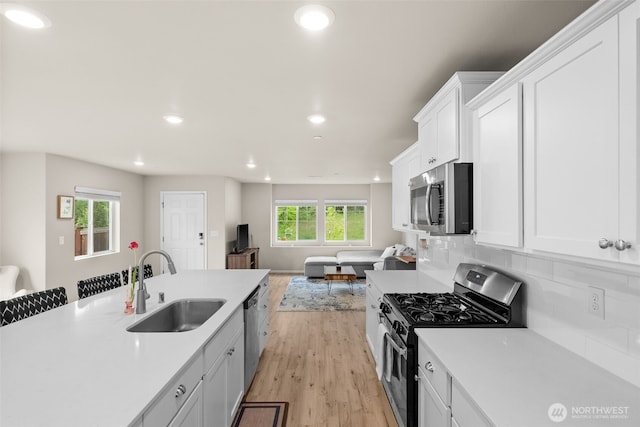 kitchen with appliances with stainless steel finishes, light wood-type flooring, a sink, open floor plan, and recessed lighting