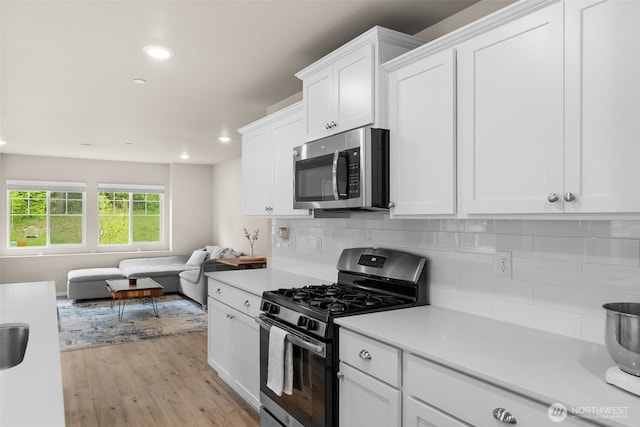 kitchen with light countertops, appliances with stainless steel finishes, white cabinetry, and open floor plan