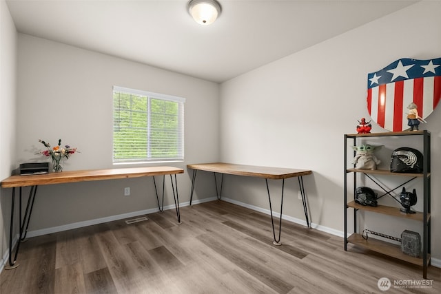 unfurnished office featuring baseboards, visible vents, and wood finished floors