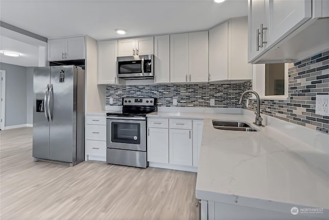 kitchen with sink, light hardwood / wood-style flooring, stainless steel appliances, light stone countertops, and white cabinets