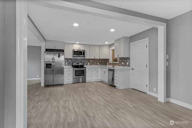 kitchen with sink, light wood-type flooring, backsplash, stainless steel appliances, and white cabinets