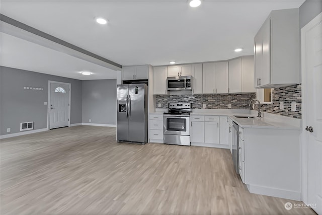 kitchen featuring sink, tasteful backsplash, white cabinetry, stainless steel appliances, and light hardwood / wood-style floors