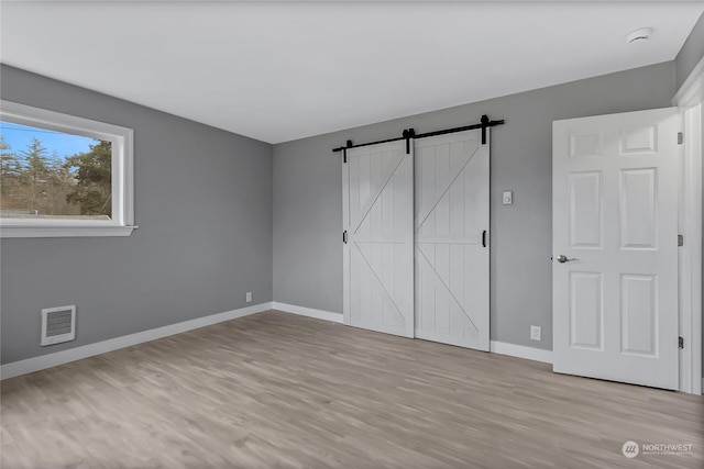 unfurnished bedroom with a barn door and light hardwood / wood-style floors
