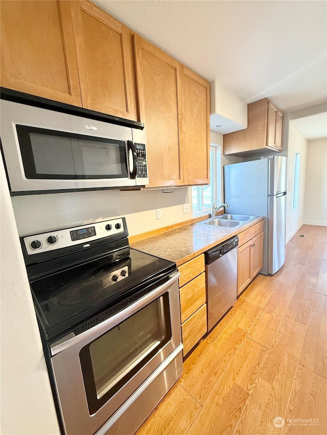 kitchen with appliances with stainless steel finishes, light brown cabinetry, sink, and light hardwood / wood-style flooring