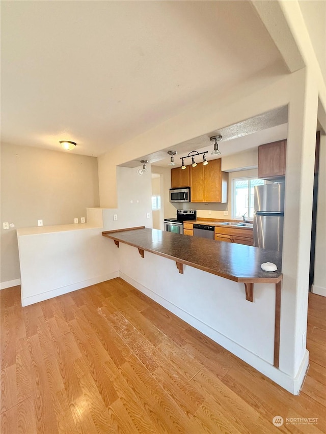 kitchen with sink, a kitchen breakfast bar, kitchen peninsula, stainless steel appliances, and light hardwood / wood-style flooring