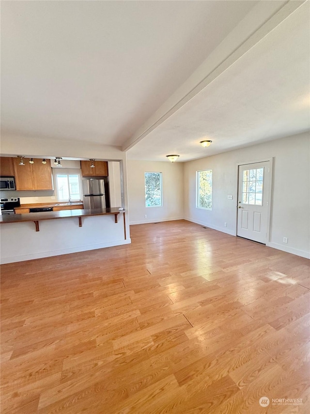 unfurnished living room featuring beamed ceiling, a healthy amount of sunlight, and light wood-type flooring