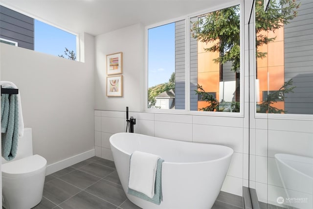 bathroom featuring a washtub, plenty of natural light, tile patterned floors, and toilet