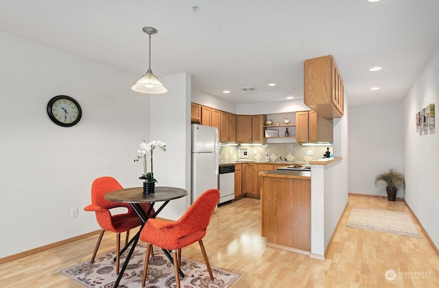 kitchen with pendant lighting, decorative backsplash, stainless steel dishwasher, kitchen peninsula, and white fridge