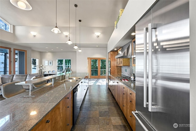 kitchen with sink, backsplash, appliances with stainless steel finishes, wall chimney range hood, and pendant lighting