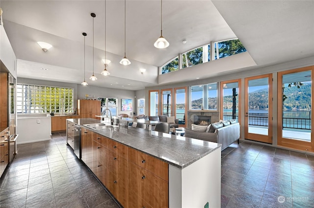 kitchen with an island with sink, hanging light fixtures, sink, stainless steel dishwasher, and high vaulted ceiling