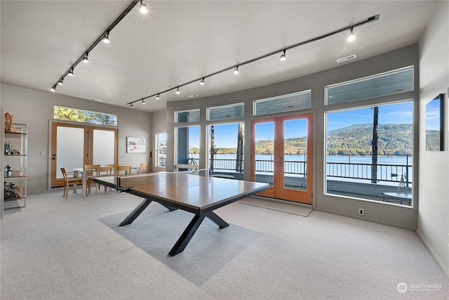 recreation room with french doors, light colored carpet, a water and mountain view, and track lighting