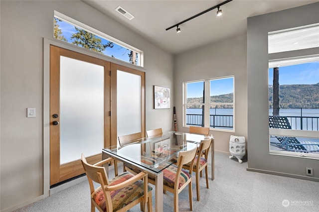 dining room with a water view, light colored carpet, and track lighting