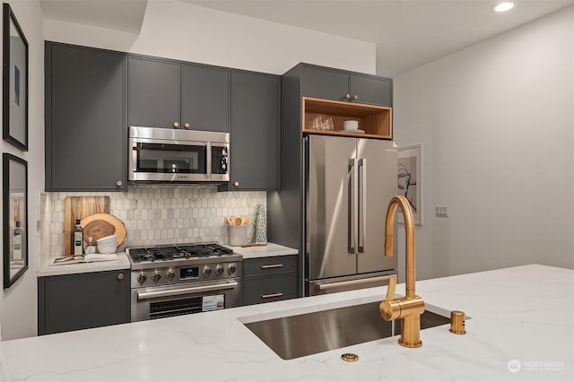 kitchen with sink, gray cabinets, backsplash, stainless steel appliances, and light stone counters